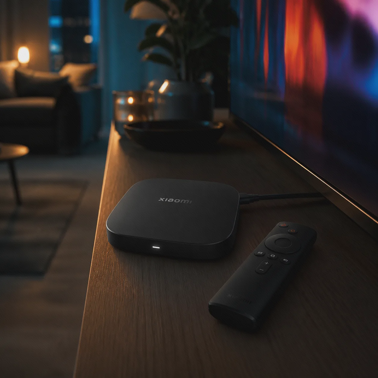 اندروید باکس مشکی Xiaomi TV Box S نسل سوم و کنترل آن روی میز چوبی کنار تلویزیون در اتاق سینمای خانگی