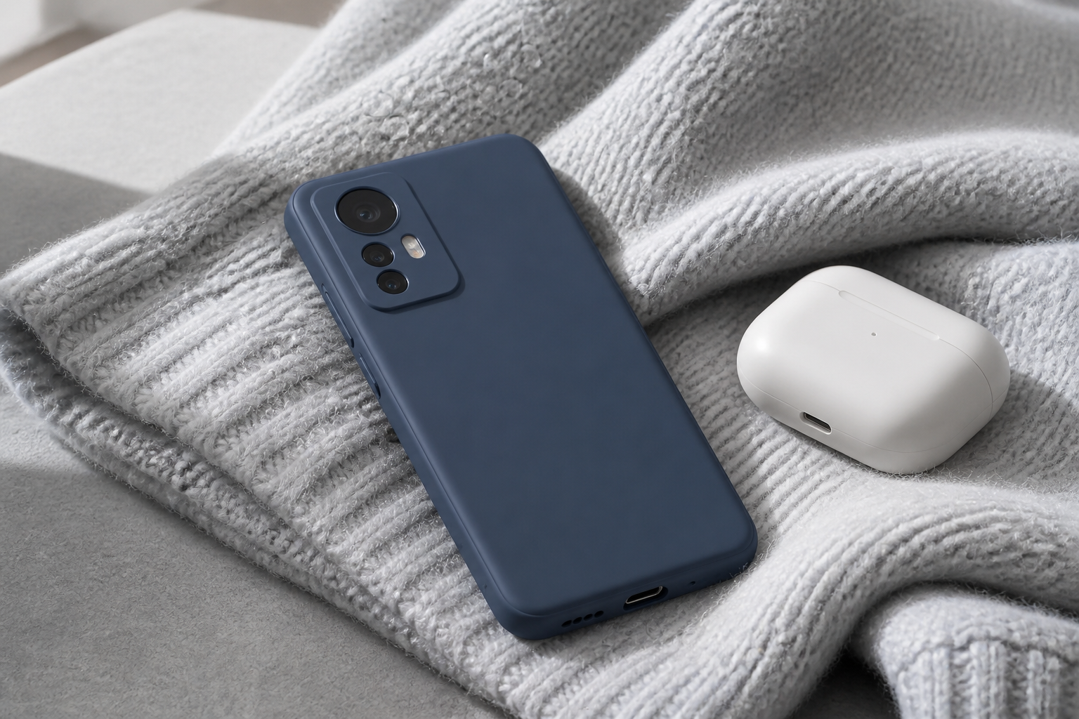 کاور سیلیکونی سرمه‌ای نصب‌شده روی Xiaomi 12 کنار هندزفری روی بافت خاکستری