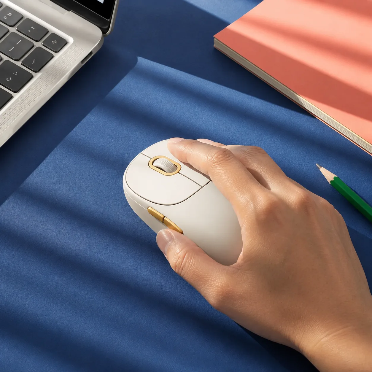 کار روزانه با موس بی سیم شیائومی Wireless Mouse 3 موس سفید Xiaomi Wireless Mouse 3 با جزئیات طلایی زیر دست روی میز کار آبی و دفتر مرجانی