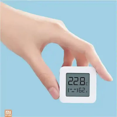 اندازه کوچک سنسور Xiaomi LYWSD03MMC در کف دست سنسور دما و رطوبت LYWSD03MMC شیائومی در دست با نمایش ۲۲٫۸ درجه