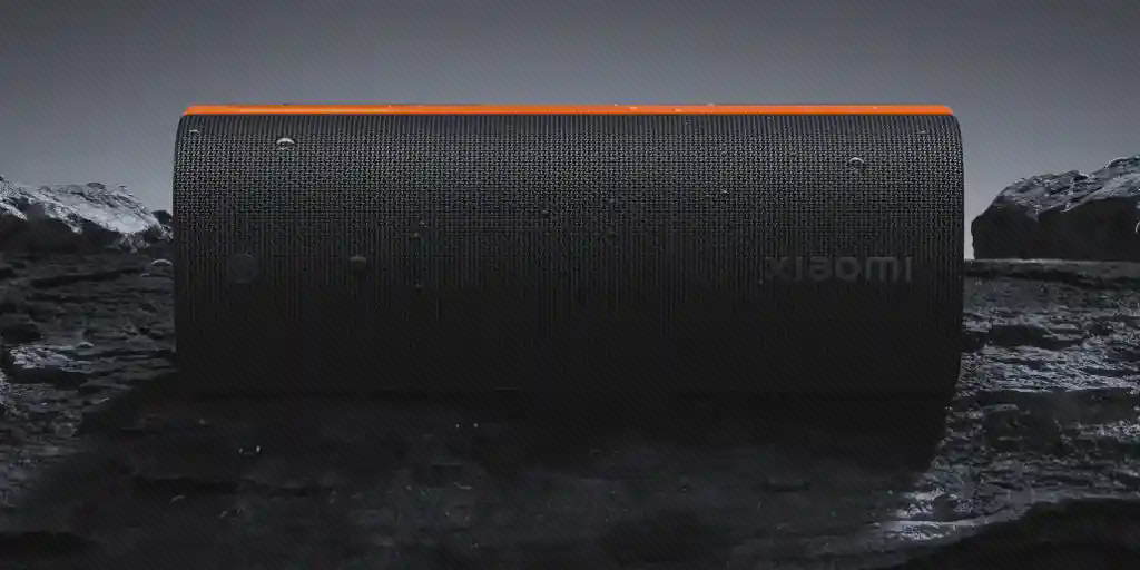 اسپیکر Xiaomi Sound Party روی سطح خیس اسپیکر مشکی Xiaomi Sound Party با نوار نارنجی روی صخره خیس در فضای تیره