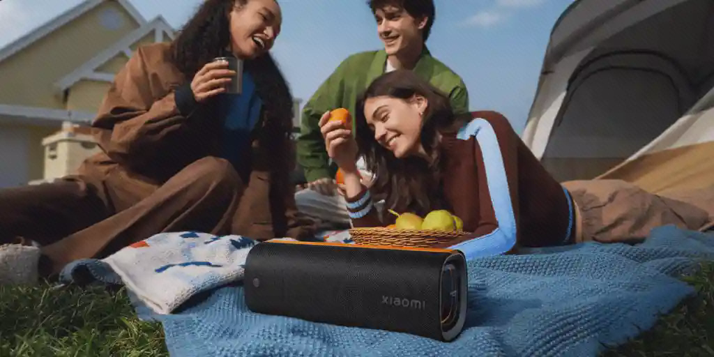 اسپیکر Xiaomi Sound Party در فضای کمپ اسپیکر Xiaomi Sound Party روی زیرانداز در کنار چادر و گروه دوستان در فضای باز