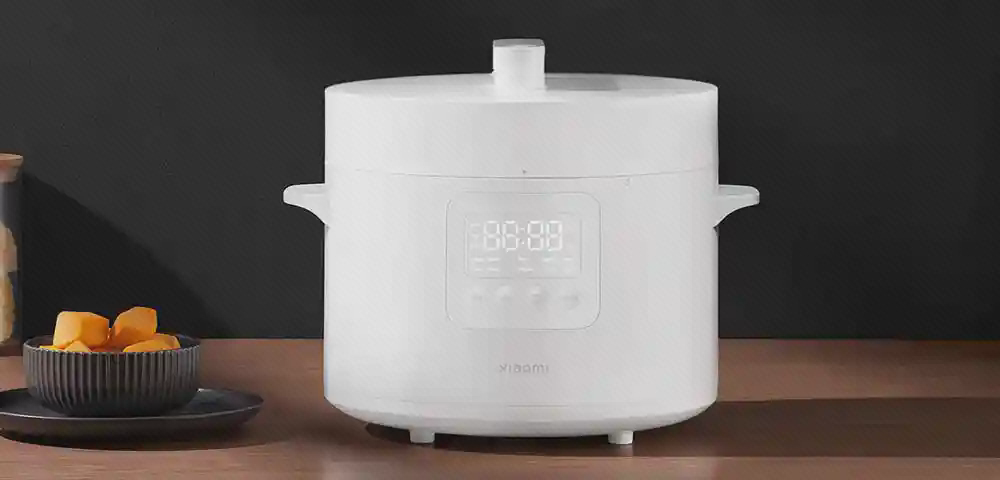 زودپز سفید Xiaomi MYL02-1 با در بسته زودپز سفید Xiaomi MYL02-1 با در بسته و نمایشگر روشن روی میز چوبی کنار ظروف غذا