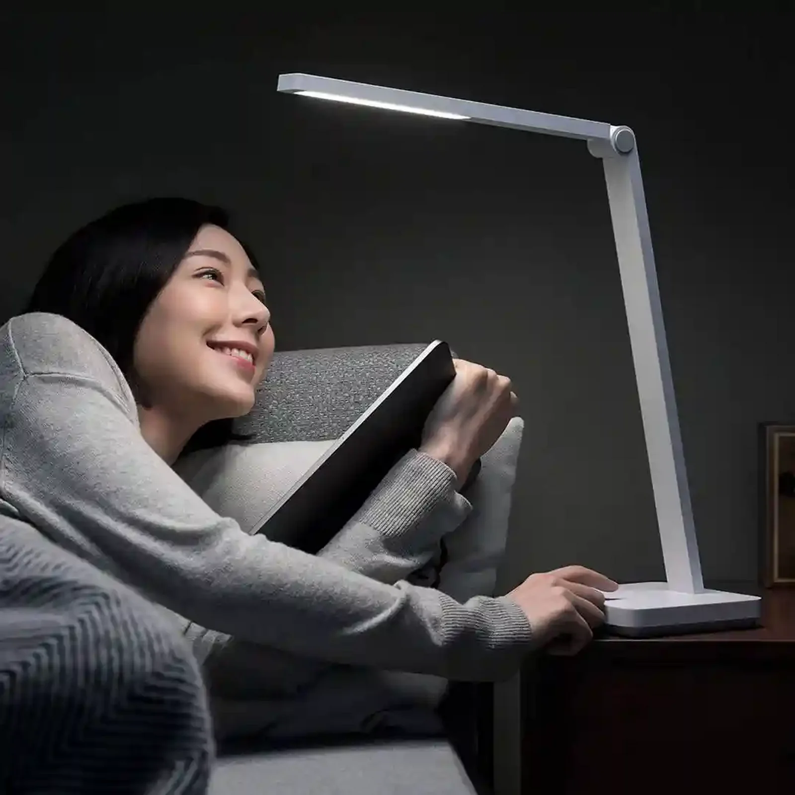 زن در حال مطالعه کتاب روی مبل کنار چراغ روشن Mijia Table Lamp Lite و دست روی پایه