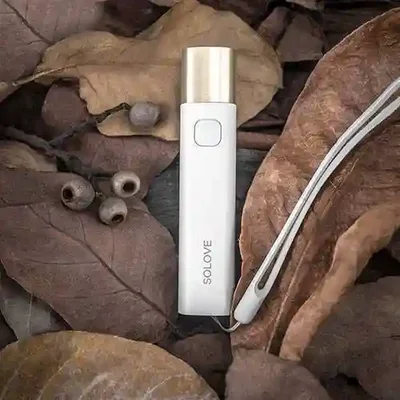 چراغقوه قابل حمل Solove X3s در فضای طبیعت چراغقوه سفید Solove X3s روی برگهای خشک با بند کناری