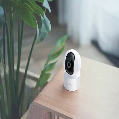 کاربرد دوربین هوشمند شیائومی C200 در فضای خانه دوربین نظارتی Xiaomi C200 روی میز چوبی کنار گیاه