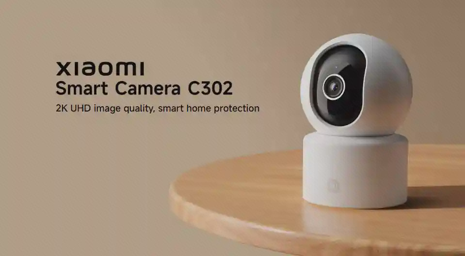 پوستر معرفی Xiaomi Smart Camera C302 دوربین سفید شیائومی C302 روی میز در پوستر معرفی با زمینه کرم