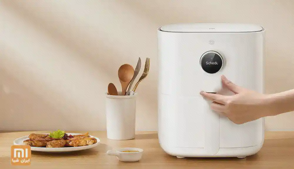 کنترل گرد هواپز Xiaomi MAF02 در آشپزخانه دست فرد روی کنترل گرد هواپز سفید Xiaomi MAF02 کنار بشقاب غذا و ظرف قاشقها