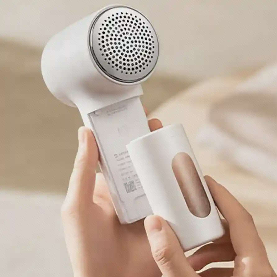 نمای بدنه باز Mijia Lint Remover 2 پرزگیر سفید Mijia Lint Remover 2 در دو دست، با بخش پشتی باز و صفحه گرد مشبک رو به بالا