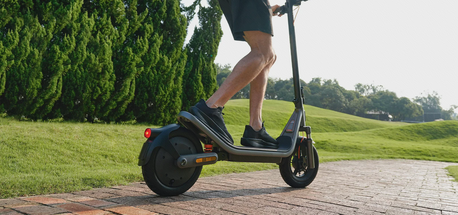 نمای جانبی پاهای راکب روی اسکوتر برقی Xiaomi Scooter 6 در مسیر سنگ‌فرش کنار فضای سبز