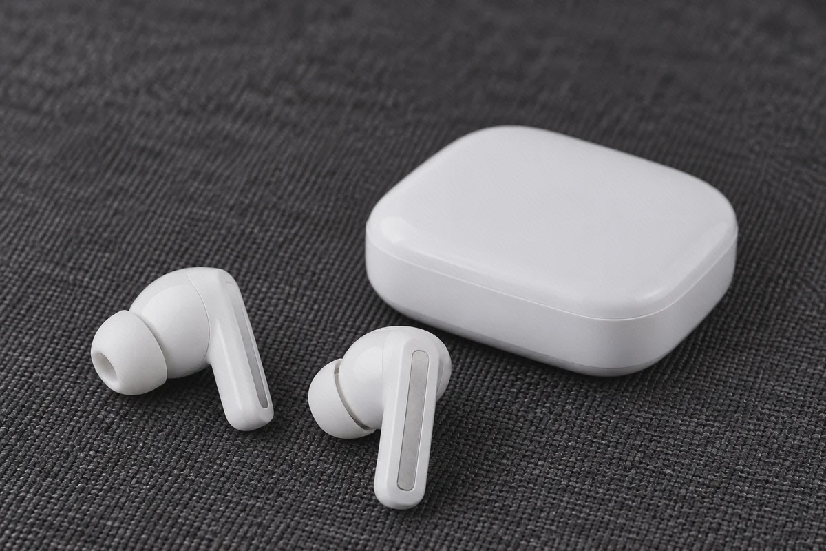 سری و ساقههای Redmi Buds 5 سفید دو گوشی سفید Redmi Buds 5 با سری سیلیکونی و جزئیات نقرهای کنار کیس بسته روی پارچه تیره