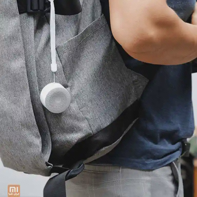 اسپیکر سفید Mi Compact Speaker 2 با بند سفید به کولهٔ خاکستری کاربر آویخته شده