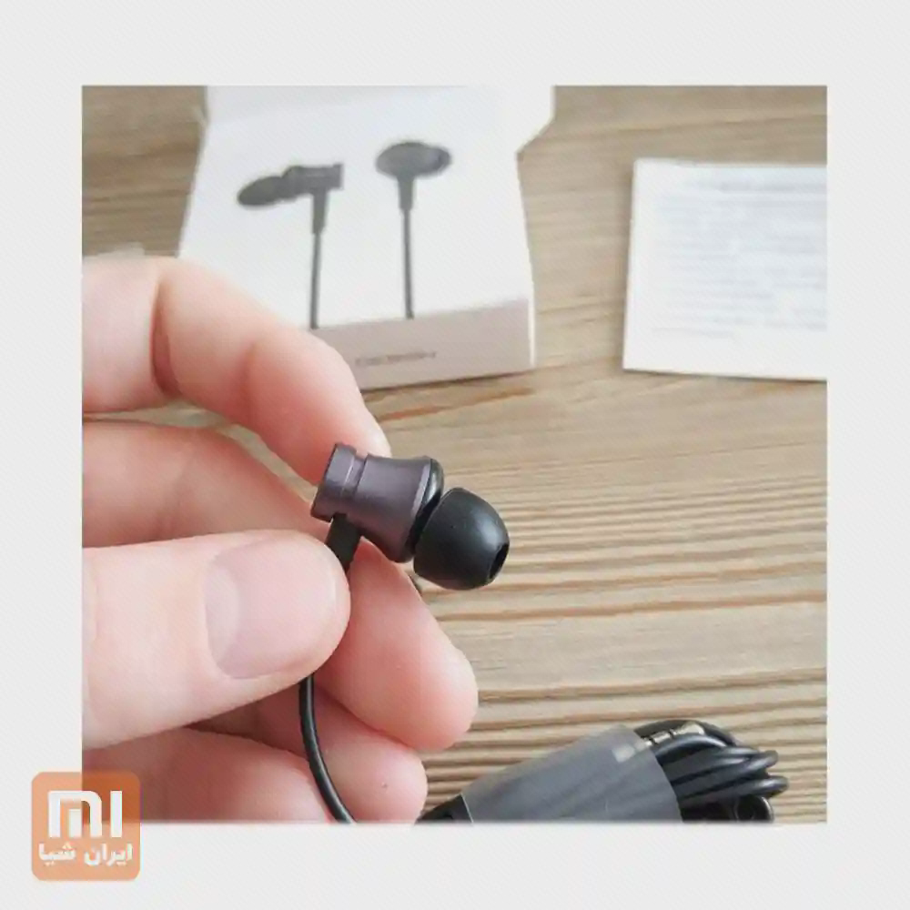 نمای نزدیک ایرباد سیمی Mi In-Ear Basic در دست با سری مشکی و جعبه در پس‌زمینه