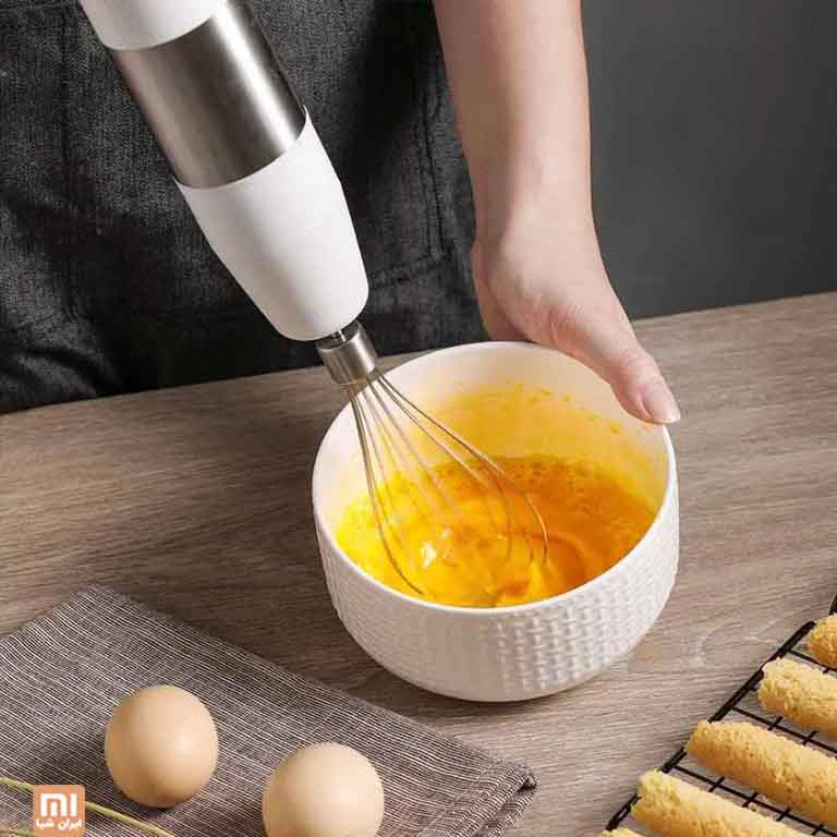 همزن بالونی CD-HB01 داخل کاسهٔ تخم‌مرغ روی میز چوبی و دست نگهدارندهٔ کاسه