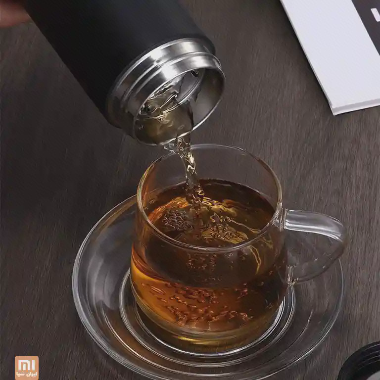 ریختن نوشیدنی از دهانهٔ فلزی فلاسک مشکی کوانژ در فنجان شیشه‌ای